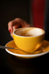 blurred woman's hand reaches for half empty yellow cup of coffee on the table