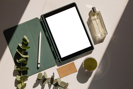 Creative space with tablet and blank screen, flowers, business card and perfume. Woman designer workspace mockup