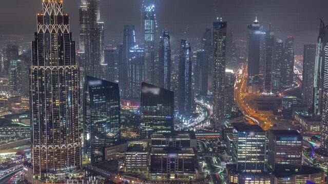 Aerial view of tallest towers in Dubai Downtown skyline and highway night timelapse. Financial district and business area in smart urban city. Skyscraper and high-rise buildings