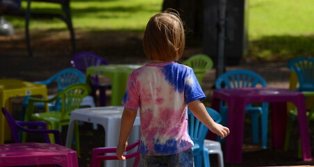 A little boy and a lot of colorful chairs. Concept: a child is waiting for guests for a birthday, children's party, friendship, loneliness.