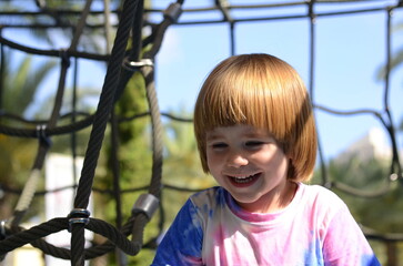 Happy boy cheering while climbing a net. Child crawling on rope mesh at playground