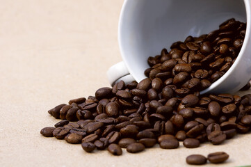 roasted coffee beans spilling white cup close up