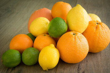 Closeup view of colorful pile of ripe citrus fruits laying on on wooden table. Solid juicy orange, grapefruit, lemon, lime, tangerine placed on brown surface. Summertime harvesting