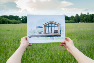Architect holding barn house  hand drawn sketch in front of a plot of land - 513147344
