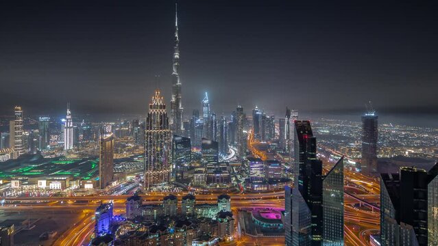 Aerial view of tallest towers in Dubai Downtown skyline and highway night timelapse. Financial district and business area in smart urban city. Many skyscrapers and high-rise buildings