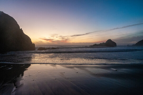 Rocks in the surf of Pfeiffer beach, around sunset. Deep yellow orange clouds color the sky.