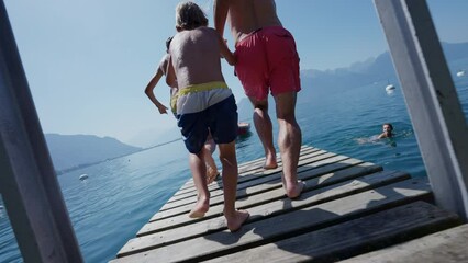 Family jumping into water father and young boys running together on pier diving into lake