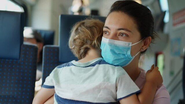 Mother wearing covid face mask holding child while travelling by train