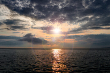 Stormy sunset over the sea. The rays of the sun through the gloomy clouds, the reflection of the...