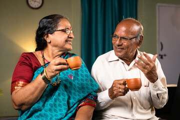Happy senior couple having tea while talking each other at home - concept of happiness, refreshment and retirement lifestyle