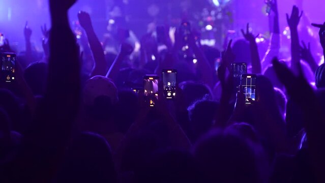 Unrecognizable fans dancing at a concert or festival party. Silhouettes of concert crowd in front of bright stage lights