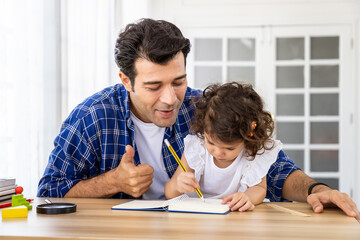 Caucasian handsome man father teach cute young preschool Caucasian child girl daughter to draw and write with pencil at desk