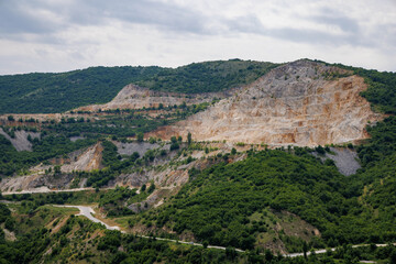 Fototapeta na wymiar Natural quarry is located near road against backdrop of Rhodope Mountains and hills with forests and mountain vegetation