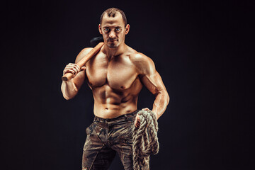 Fototapeta na wymiar One handsome sexual strong young man, muscular body holding rope and hummer on shoulder standing posing in studio on black background
