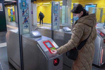 a young woman in a hygienic mask scans a card at the terminal in the subway 