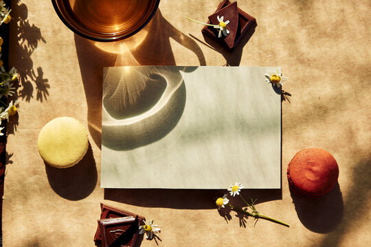Aesthetic tea time, herbal tea and macarons dessert outside in the terrace under trendy hard shadows. Mock up of stationery card for wishing, greeting, invitations or recipe