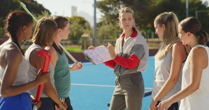 Hockey coach planning a strategy and positions with a group of teenage players on a sports pitch. Sports trainer standing with hockey team and using clipboard to show game plan to win before match