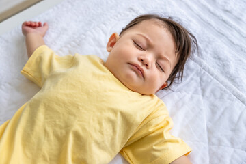 Little Asian baby girl lying down sleeping on bed at home. Newborn child relaxing in bed. Nursery for young children.