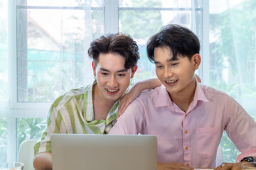 Cute Asian LGBT gay man couple, using laptop working at home, spend time together. Healthy lifestyle with orange juice.