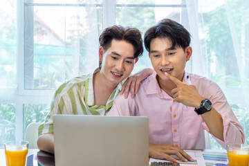 Cute Asian LGBT gay man couple, using laptop working at home, spend time together. Healthy lifestyle with orange juice.