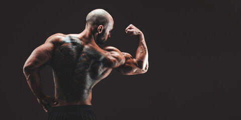 Fototapeta na wymiar BAck view of a muscular man with tattoo on back against of black background. Isolated