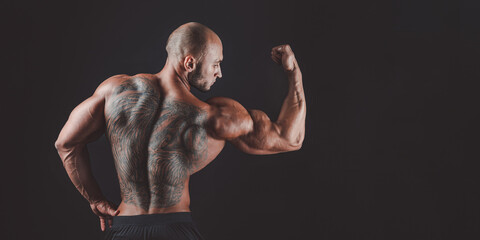 BAck view of a muscular man with tattoo on back against of black background. Isolated
