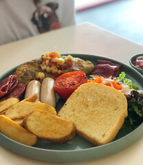 Breakfast meal with potato wedges, fries, bread, fried sausage, tomato, egg omelette and bacon beef