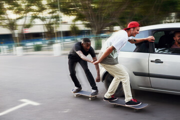 Never let your best friends do stupid things alone. Shot of two skaters holding on to a moving car.