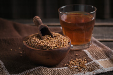 Bowl of fenugreek seeds and Egyptian fenugreek yellow tea or Methi Dana drink on dark wooden background - obrazy, fototapety, plakaty