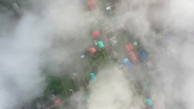 An aerial view of the village among the lush rain clouds covering the houses during the rainy season.
