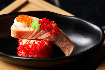 Piece of sushi ingredients: salmon, caviar, Masago, Ikura, Tobico on a black plate. Front view. Close-up Food concept