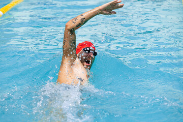 One athlete, male professional swimmer in goggles and red swimming cap swimming at public pool, at open-air. Sport, power, energy, style, hobby concept.