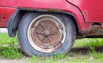 Weathered car wheel with dirt and grime. Rusty abandoned car in the parking lot. Restoration of a retro car. Flat tire. Vintage wheel with classic red car cap. - Powered by Adobe