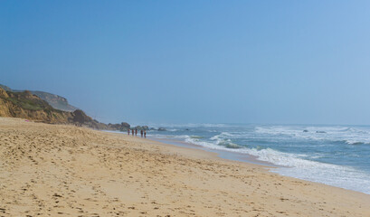 Beach by the ocean with people resting, vacation spot. Mountains, sea and waves. Travel to Europe Portugal.