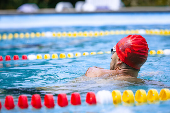 Live portrait of young sportive man, professional swimmer in goggles training at public swimming-pool, outdoors. Sport, power, energy, style, hobby concept.