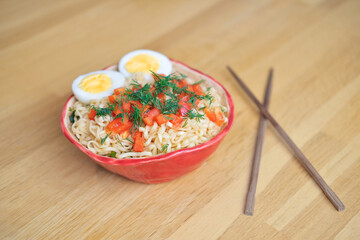 asian noodles with egg and vegetables in red bowl and chinese chopsticks  on wooden table top