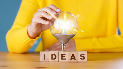 Woman touching glowing light bulb on ideas wording on wooden block for creative idea. Thinking and...