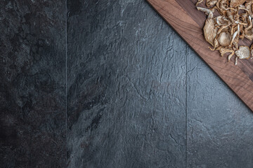 Trockenpilze auf dunklem Holzbrett, dunkler Schiefer-Untergrund, viel Freiraum