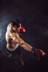 Fototapeta na wymiar Muscular kickbox or muay thai fighter punching in smoke