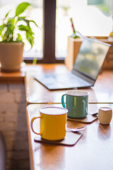 Coffee cups and laptop on the table in cafe. Coffee break. Idyllic place for work. Freelance work place. Morning with coffee and notebook. Cafe interior. Creative space for work. Hot morning drinks.