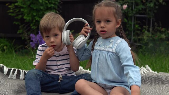 Two Happy Siblings boy ans girl listening to music on headphones outside in Garden. Children and technology. Brother and Sister. Love of music, dreams hobbies. Childhood, musicality, hobby. Friendship