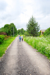 Obraz premium Children walk along the road in the village. Summer village landscape. Walking along a rural road. The road in the village.