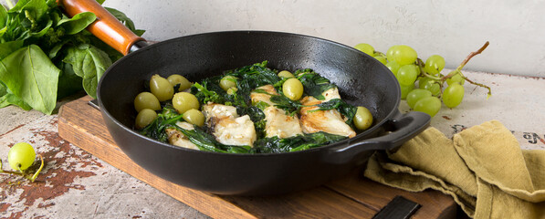 pan with fried halibut with spinach and grapes on the table