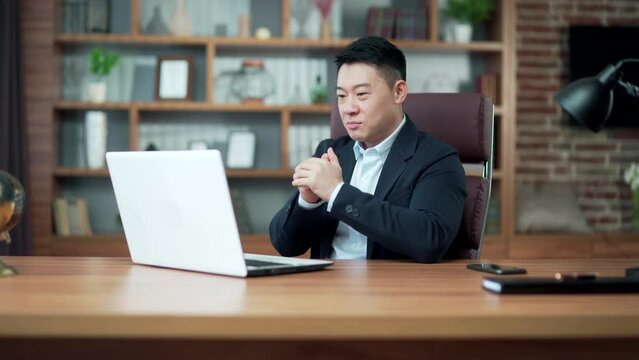 Young excitable asian man screams with joy and waves hands looks at laptop screen after winning online casino and getting jackpot sits at table in office. Gambling addiction applauds good result. Asia