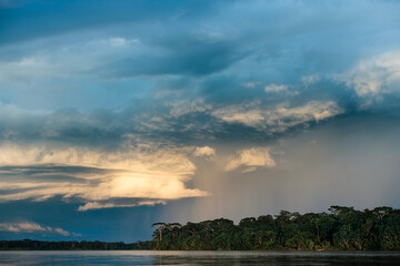 Fototapeta na wymiar a distant rain falls on the Amazon rainforest with a river in the foreground