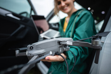 A woman sits in a car with a laptop and drone - obrazy, fototapety, plakaty