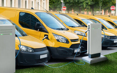 Row of yellow electric delivery vans at charging stations for electric vehicles