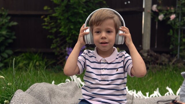 handsome smiling boy listening to music on headphones. Children and technology. Love of music, children's dreams hobbies. Talented happy little child resting outside. Childhood, musicality, hobby