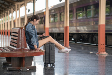 Fototapeta na wymiar Asian young woman traveler sitting in a train station and using a digital tablet. Travel concept.