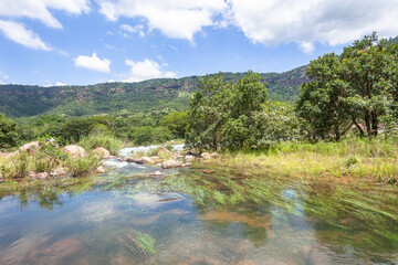 Fototapeta na wymiar River Tributary Flowing Clean Flowing Water Rocks Tropical Valley Landscape.